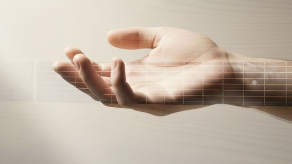 Guitarist demonstrating a relaxed hand grip on a fretborard overlay to prevent guitar hand tension while 