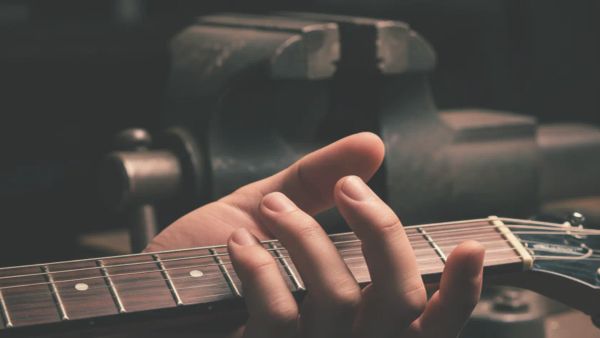 a hand tightly gripping guitar neck, in the background a vice representing the force of the grip 