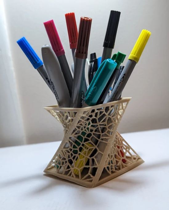 Image of a 3d printed voronoi vase in a light tan color, filled with multiple markers