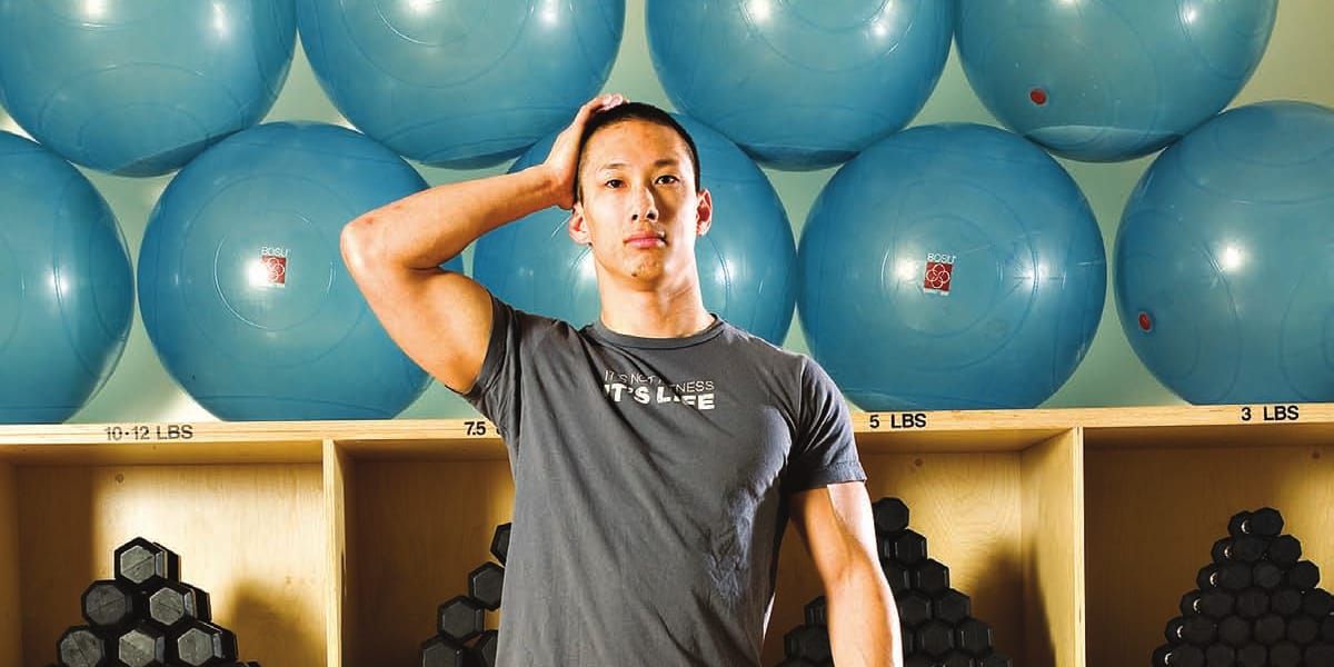 Andrew Nguyen demonstrating gentle side-of-head isometric resistance in a gym.