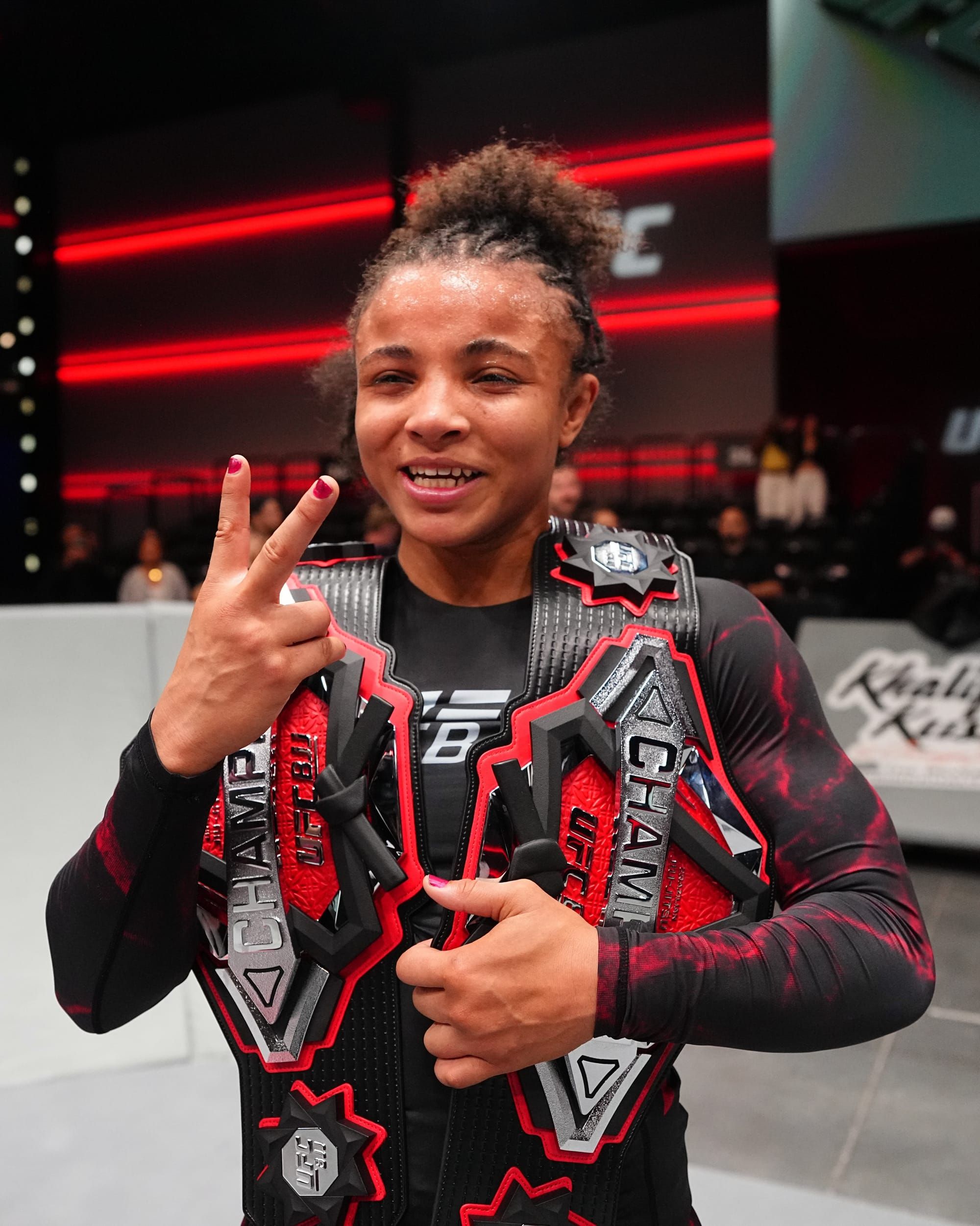 Cassia Moura smiling while holding two UFC BJJ championship belts after UFC BJJ 12.
