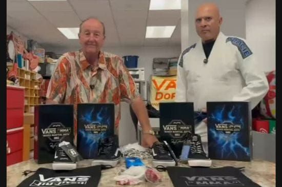 Royce Gracie wearing a white gi beside Steve Van Doren, with Vans jiu-jitsu and MMA branded shoes, boxes and apparel.