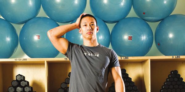 Andrew Nguyen demonstrating gentle side-of-head isometric resistance in a gym.