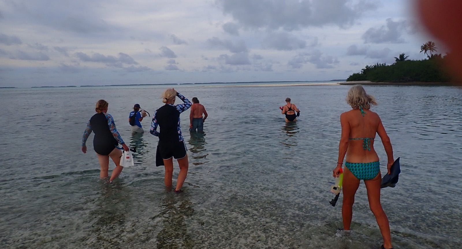 Snorkellers wading out across a shallow lagoon at dusk