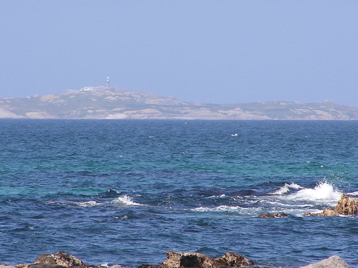 Barunguba Montague Island seen across deep blue water from the rocks at Narooma, the lighthouse small on its ridge
