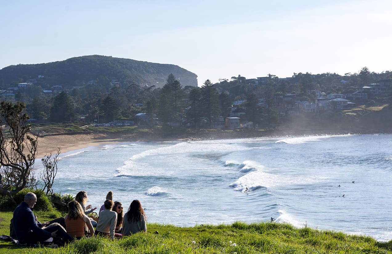 Friends with their coffees on the headland grass above Avalon Beach
