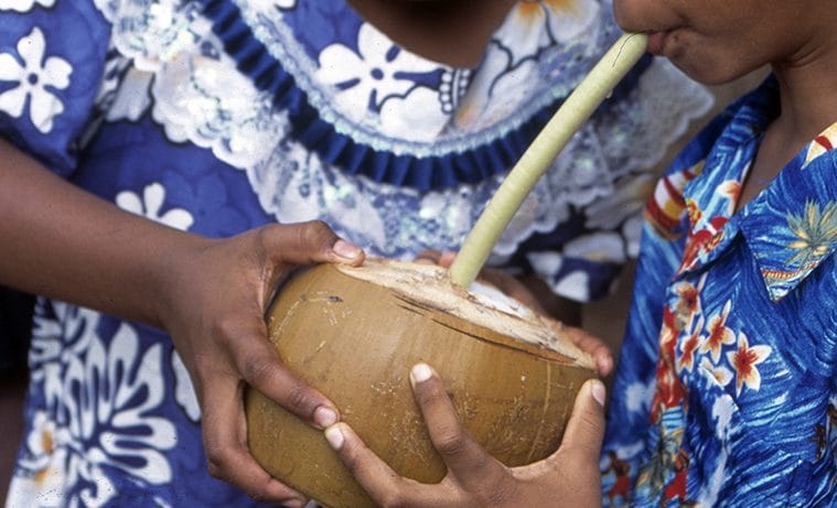 Two children sharing a green coconut through a natural straw