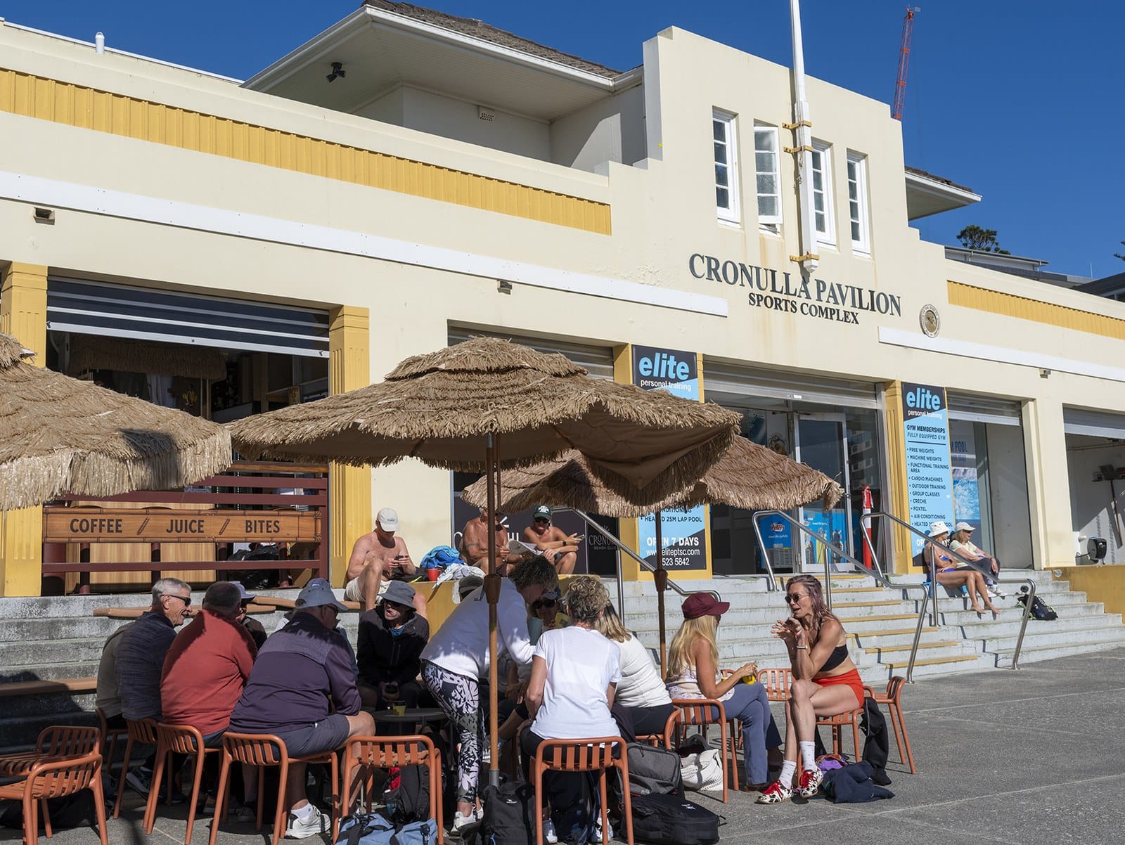 Cronulla Pavilion on the beachfront, cafe umbrellas and people on the steps