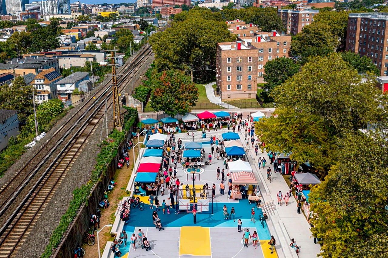 A market day on the two courts at the South Jamaica Houses in Queens, seen from above, with the housing blocks and a rail line beside them