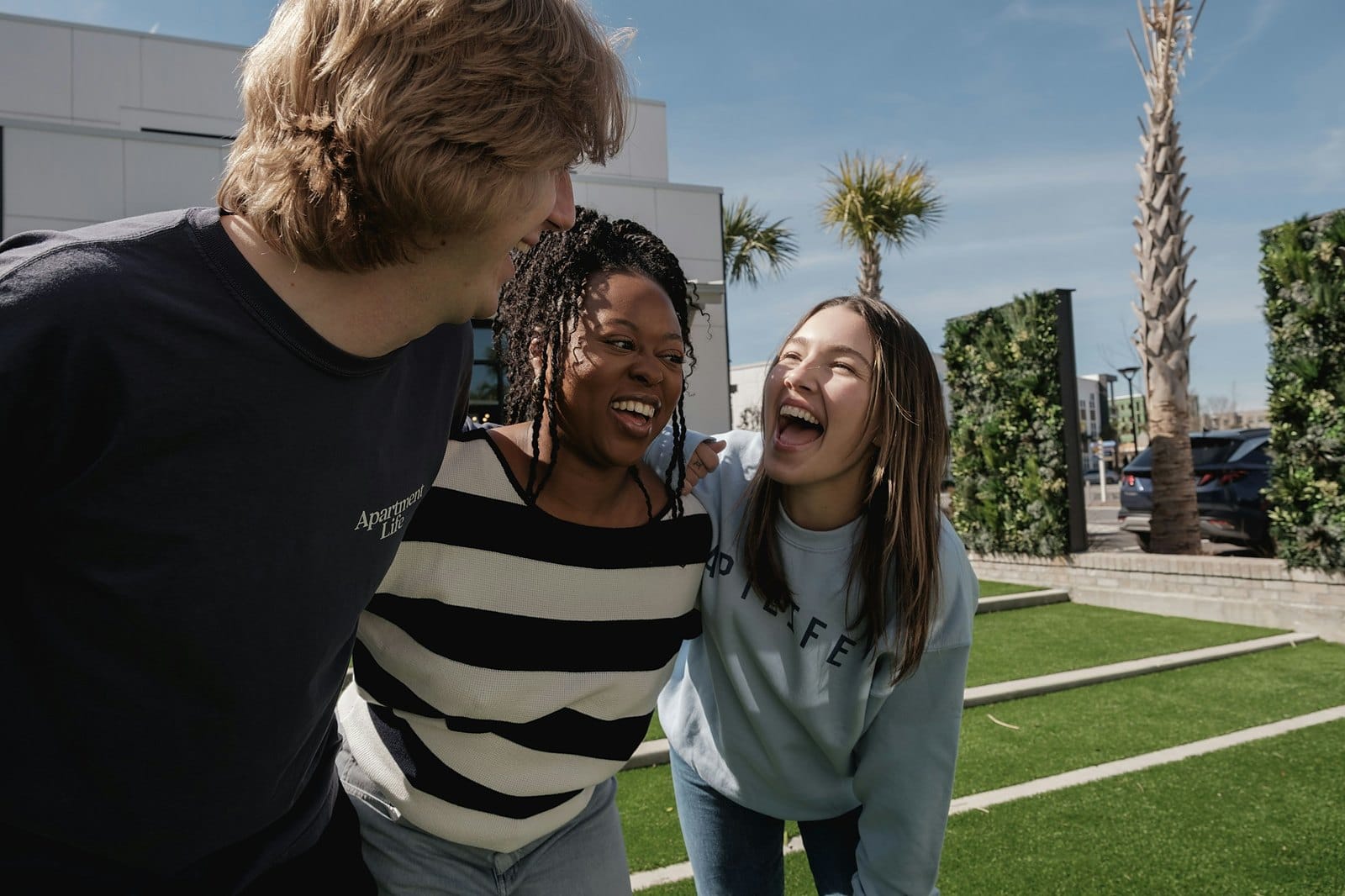 Three friends laughing together outdoors on a sunny day