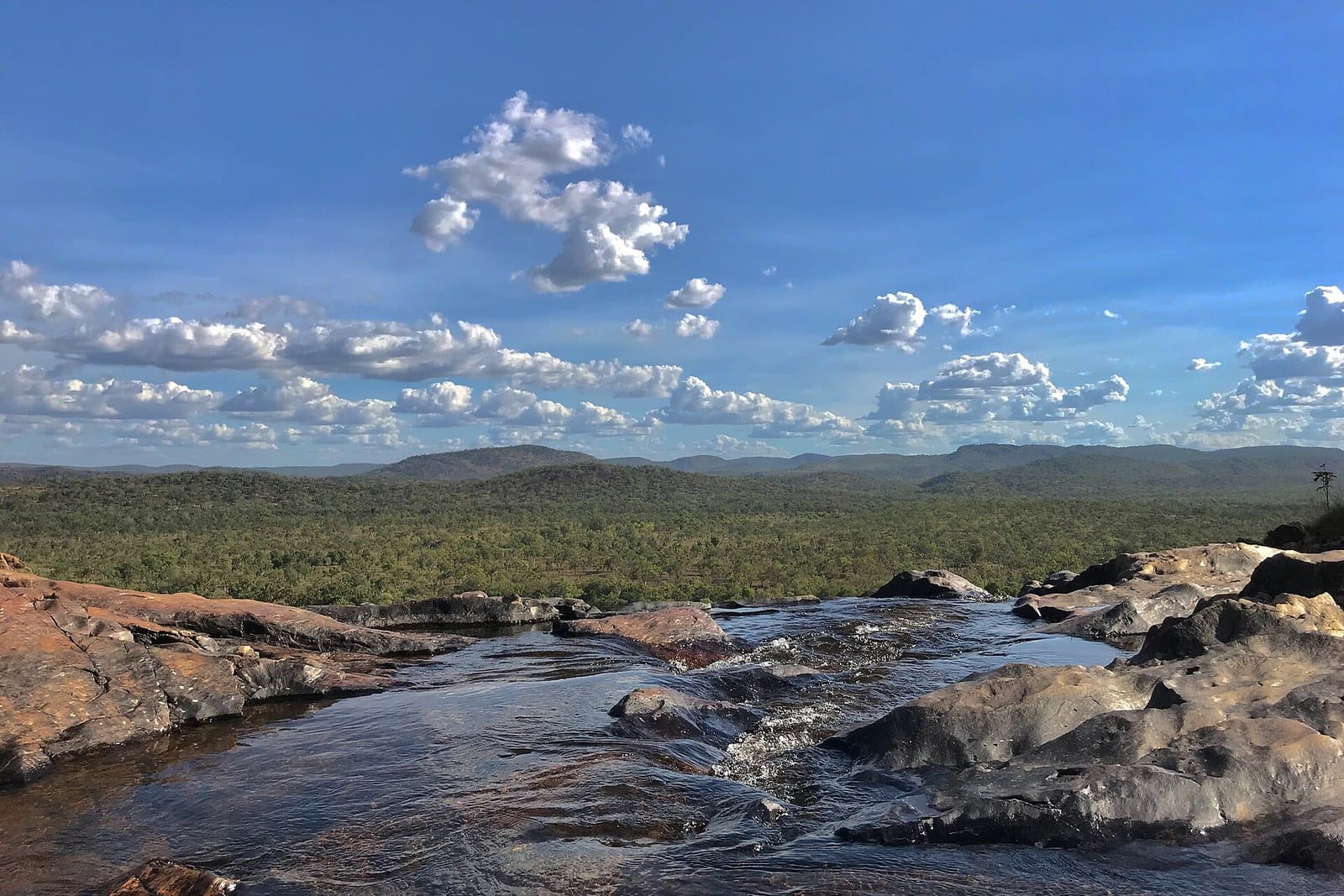The rock pool at the top of Gunlom Falls looking out over Kakadu under a blue sky with white clouds