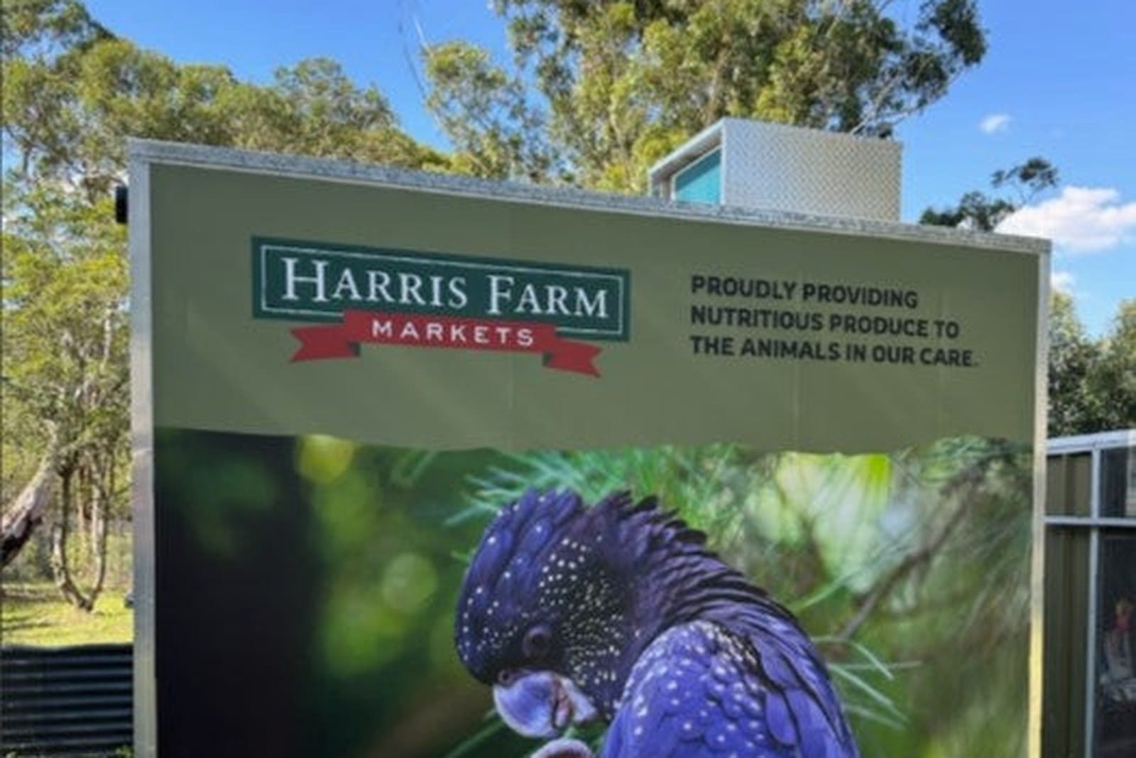 A Harris Farm Markets sign with a black cockatoo picture standing in bushland