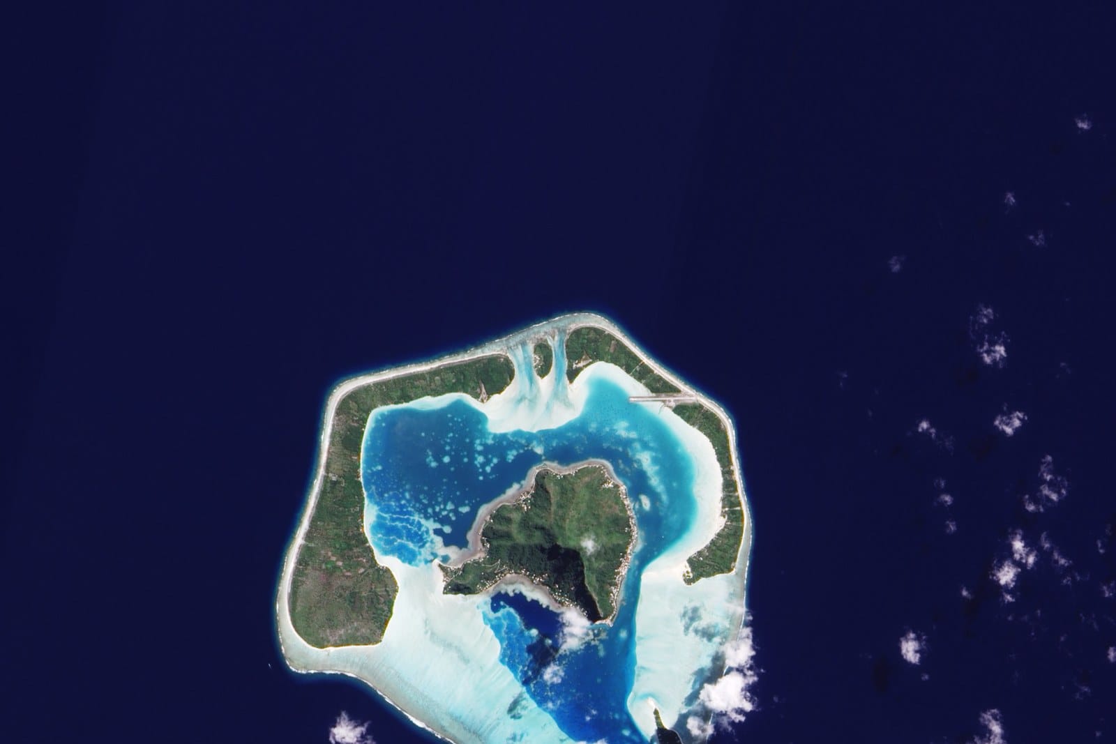 Maupiti from space, a green island inside a pale lagoon in deep blue ocean
