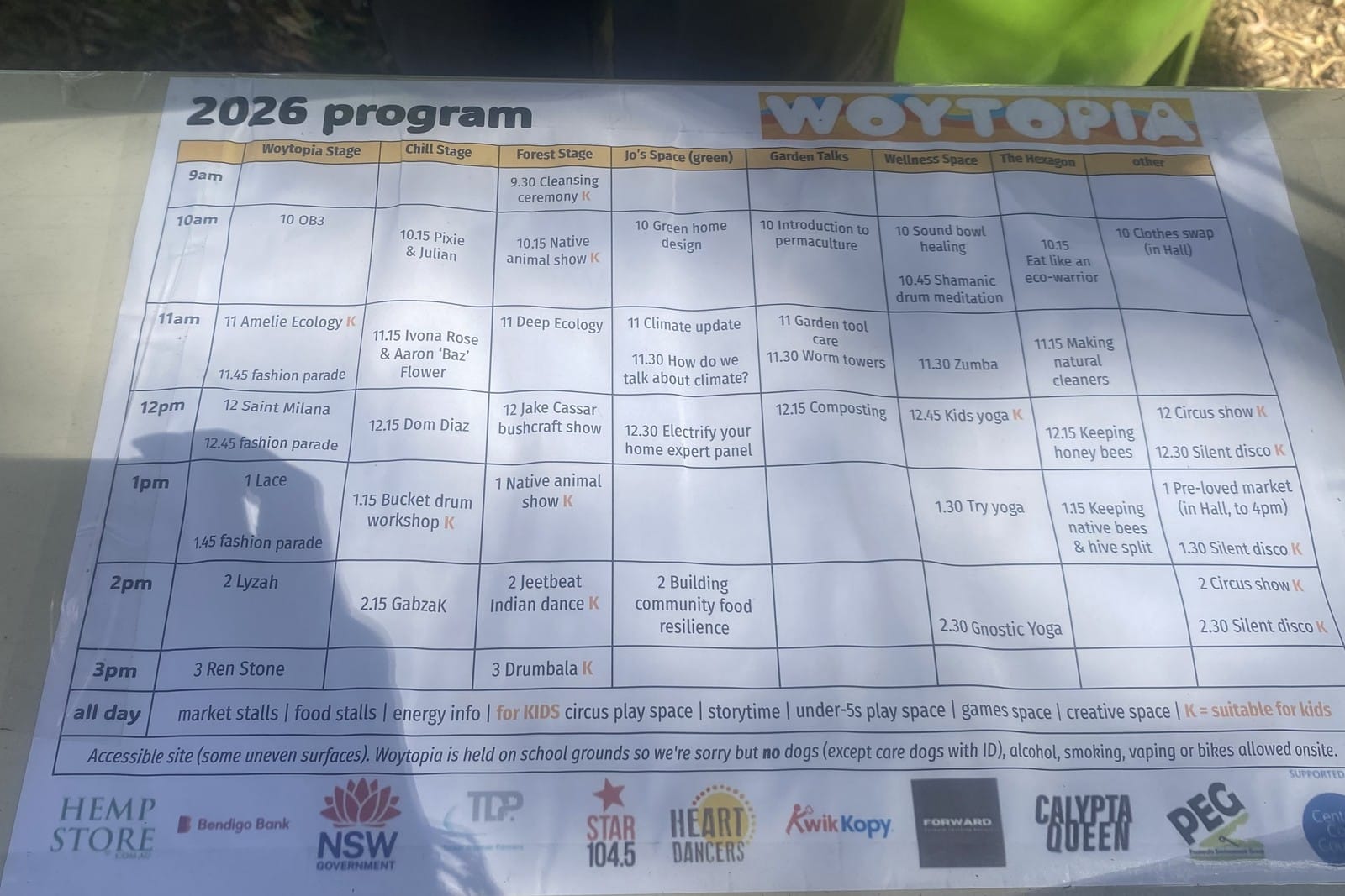 A printed festival program grid on a sheet of paper lying on the grass