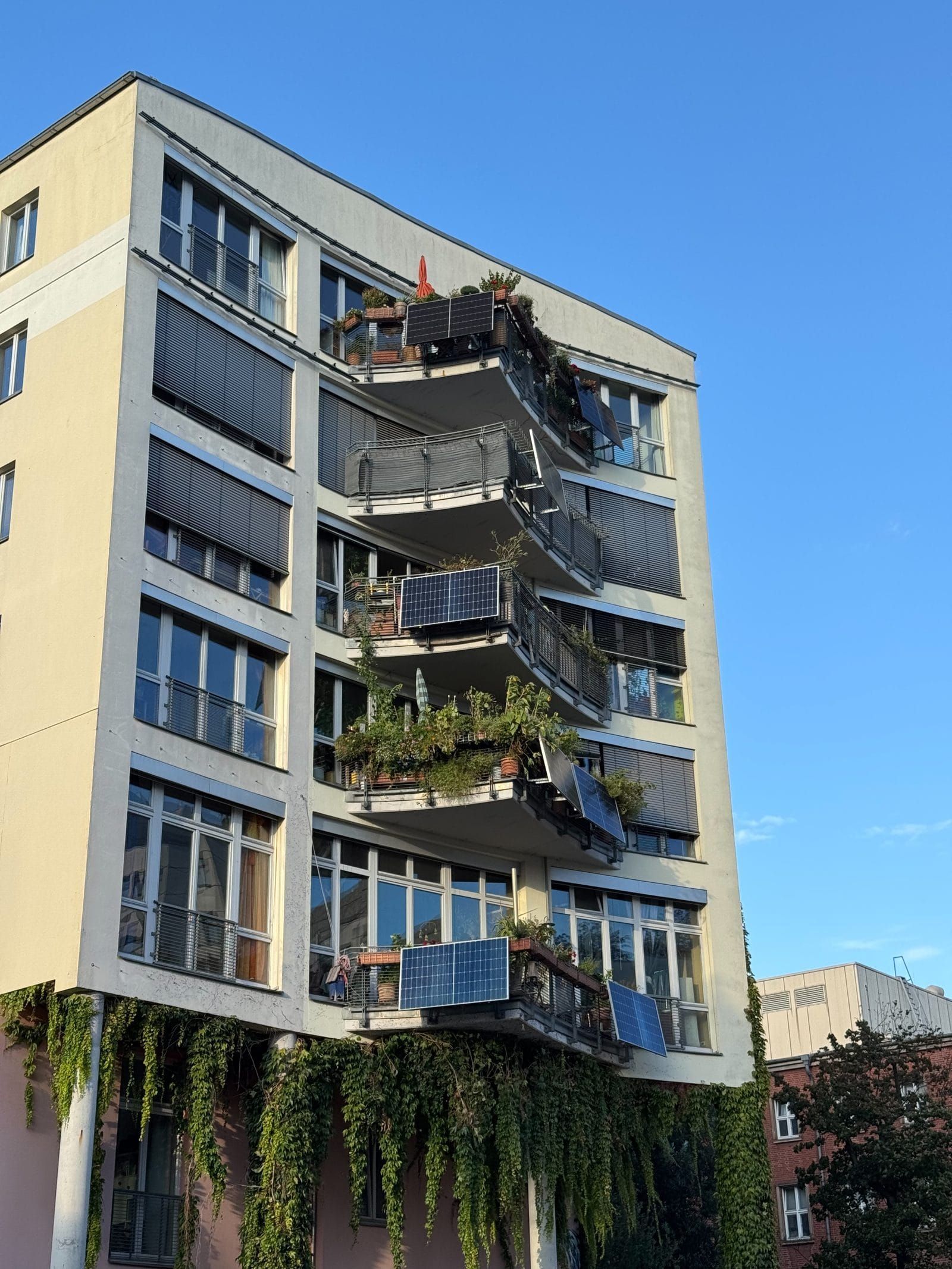 A German apartment building with solar panels hanging from balconies full of plants