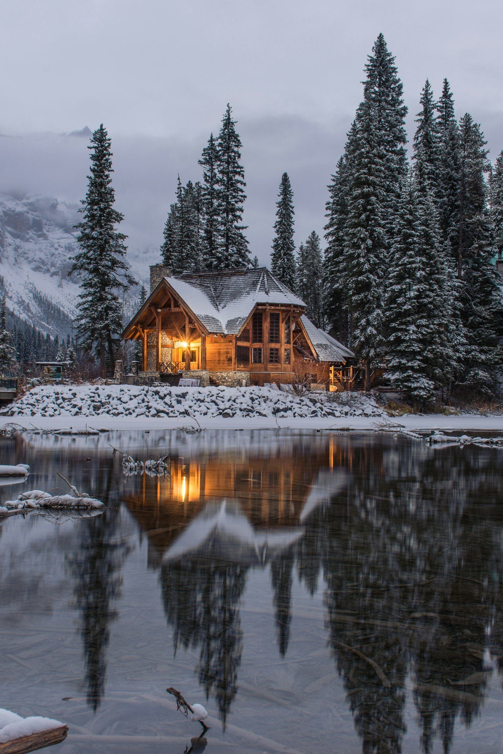A timber house glowing warmly beside a lake on a snowy evening