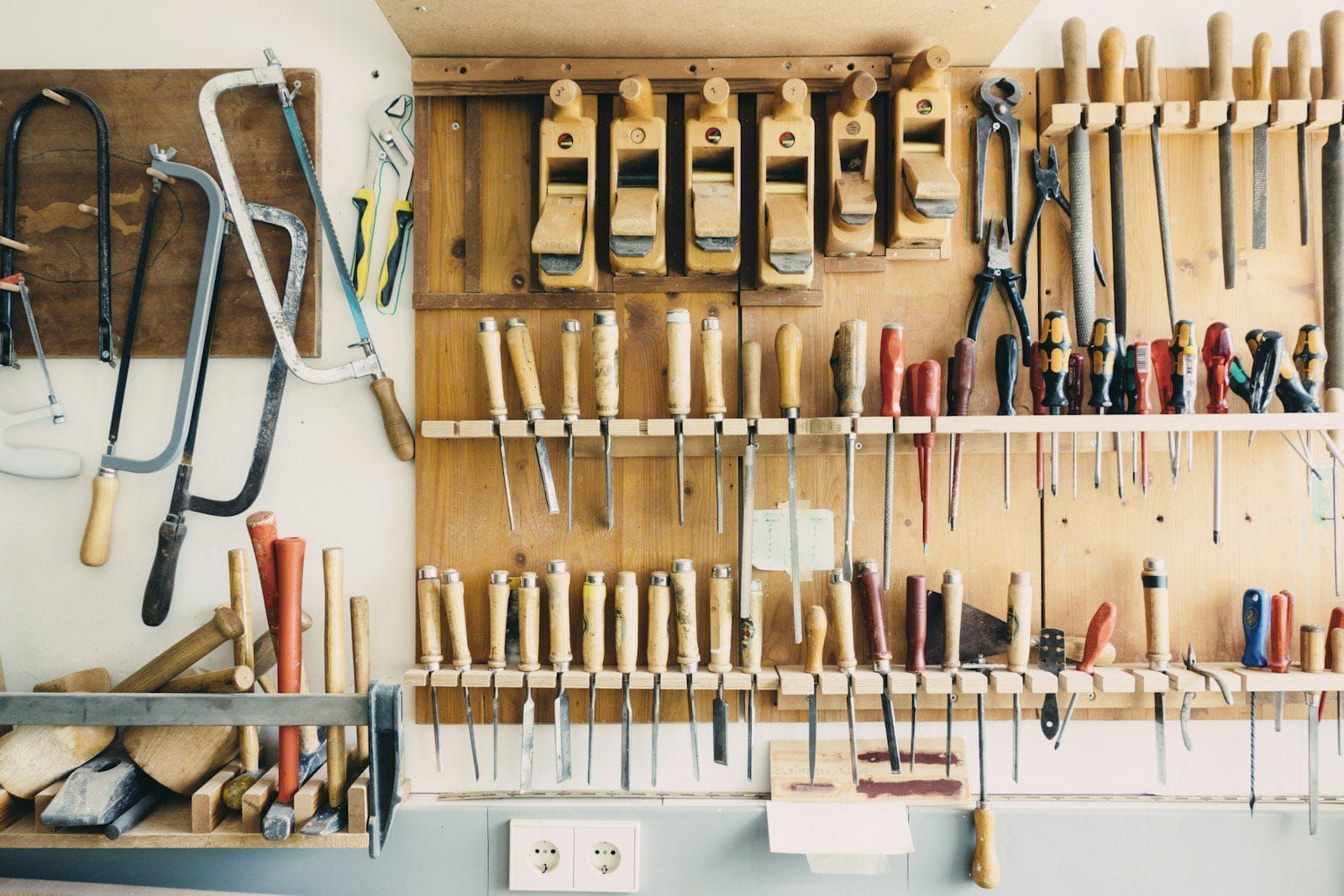 A wall of well kept hand tools hung neatly on a light wooden workshop wall