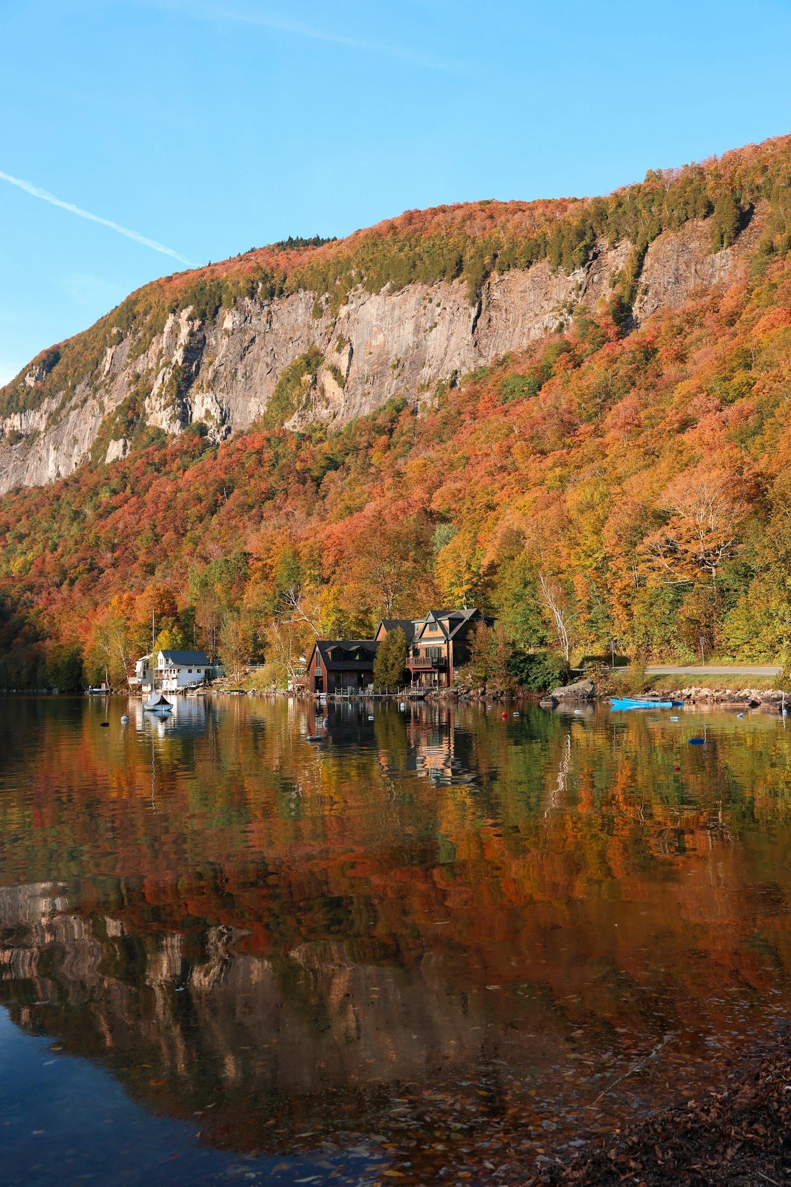 A forested hillside in autumn colour reflected in a still Vermont lake