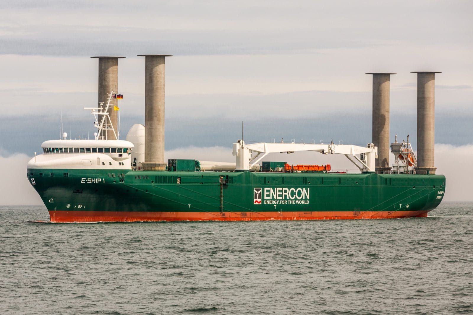 E Ship 1, a green hulled cargo ship with four tall grey rotor sail cylinders standing on her deck, at sea