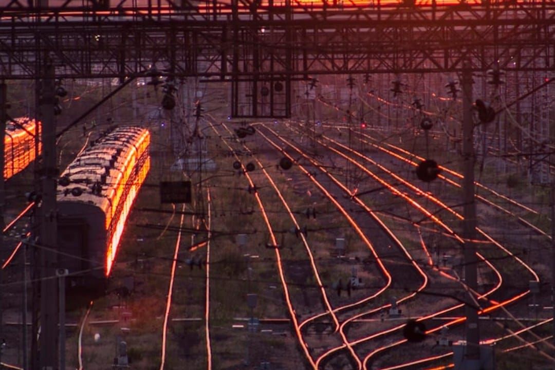 Railway tracks fanning out at sunset, the rails lit orange by low sun