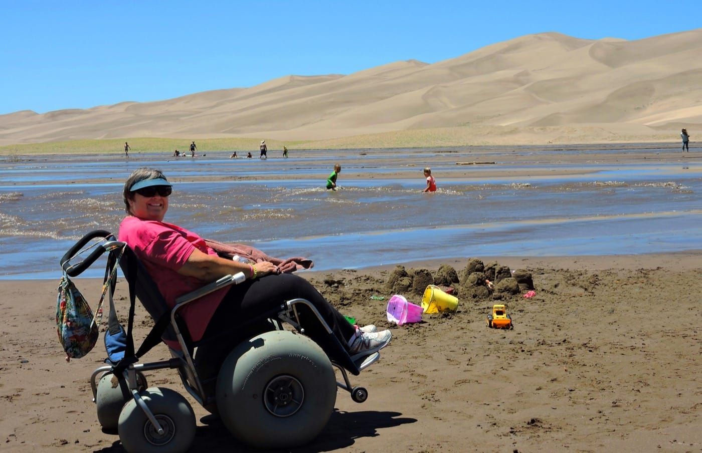 A woman in a beach wheelchair beside a creek at Great Sand Dunes National Park