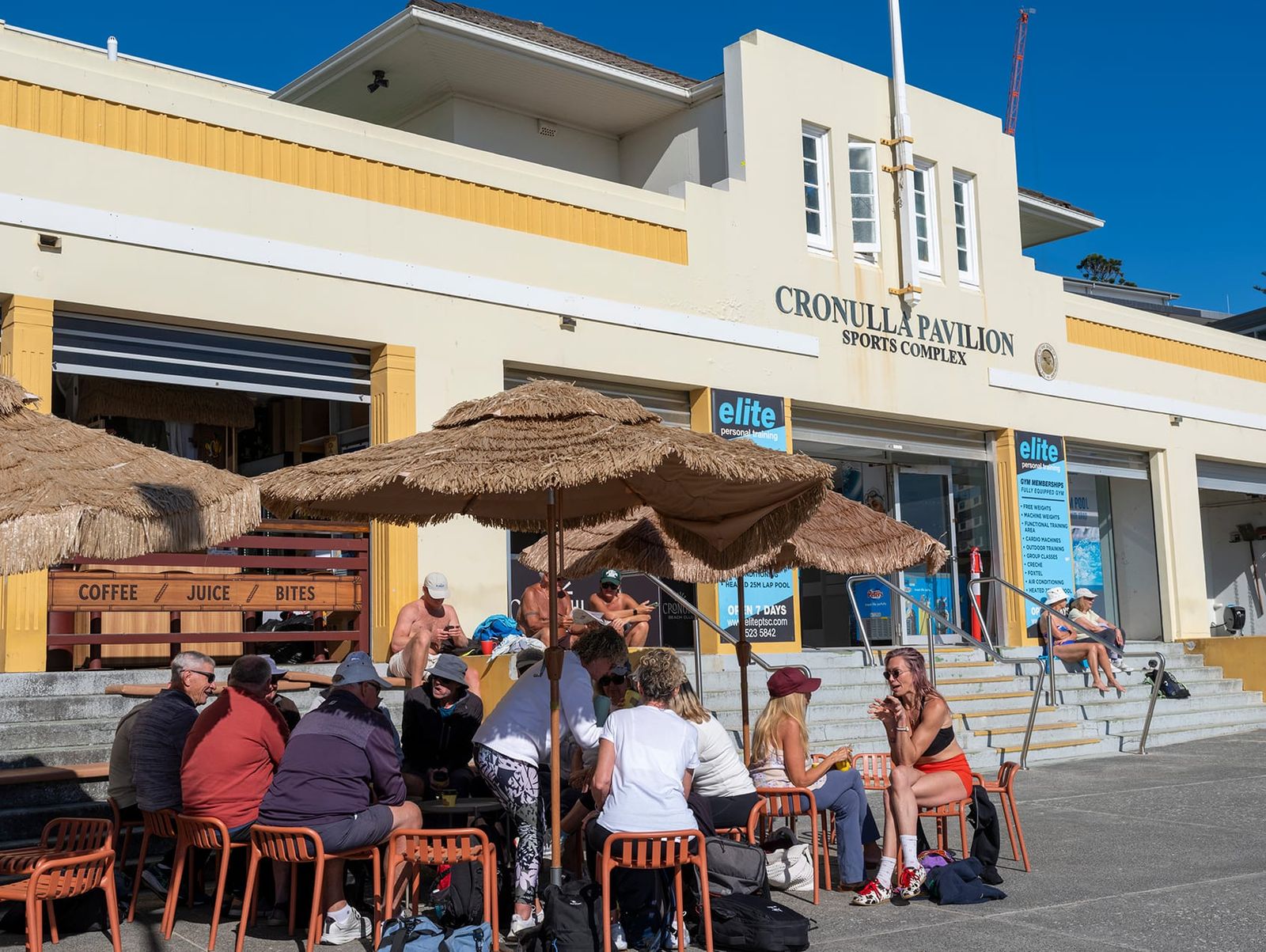Cronulla Pavilion on the beachfront, with cafe umbrellas and people on the steps