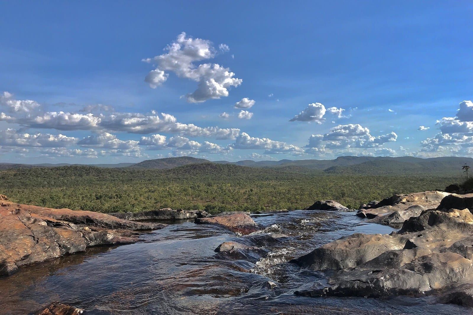 The rock pool at the top of Gunlom Falls looking out over Kakadu under a blue sky with white clouds