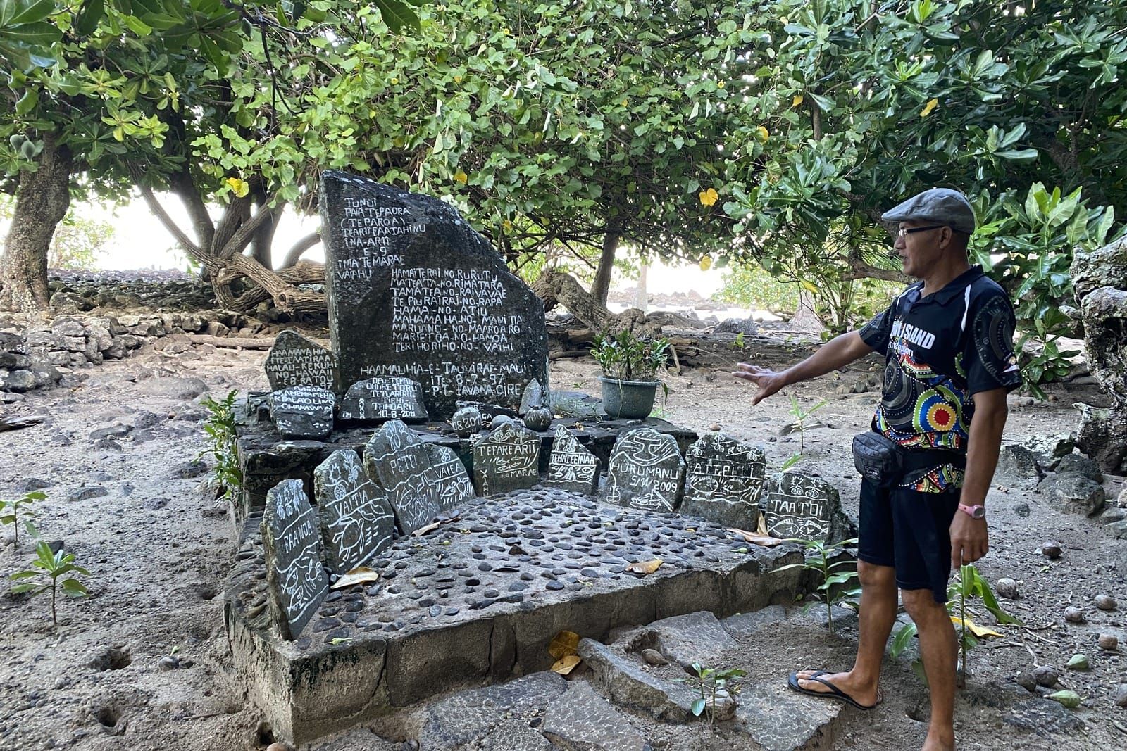 Jeffrey Tamati standing beside the nine carved sustainability stones under trees at Marae Vaiahu, Maupiti