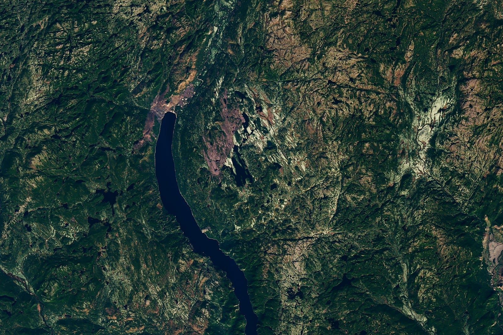 Satellite view of a faint circular depression in green boreal forest dotted with lakes