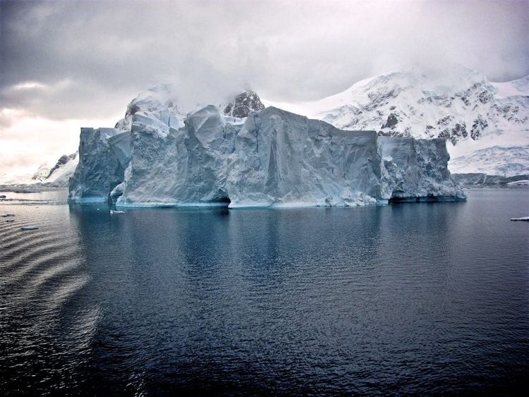 A large iceberg with snow covered mountains behind it in Antarctic waters