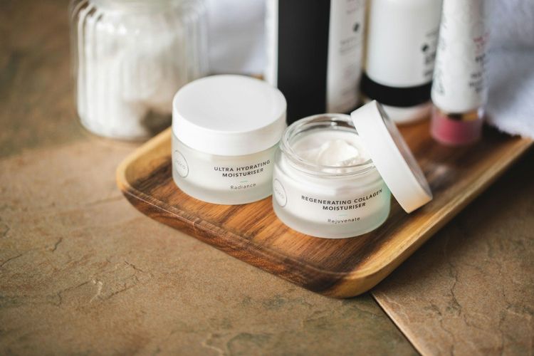 Cream jars with white lids arranged on a wooden tray, a stand in image