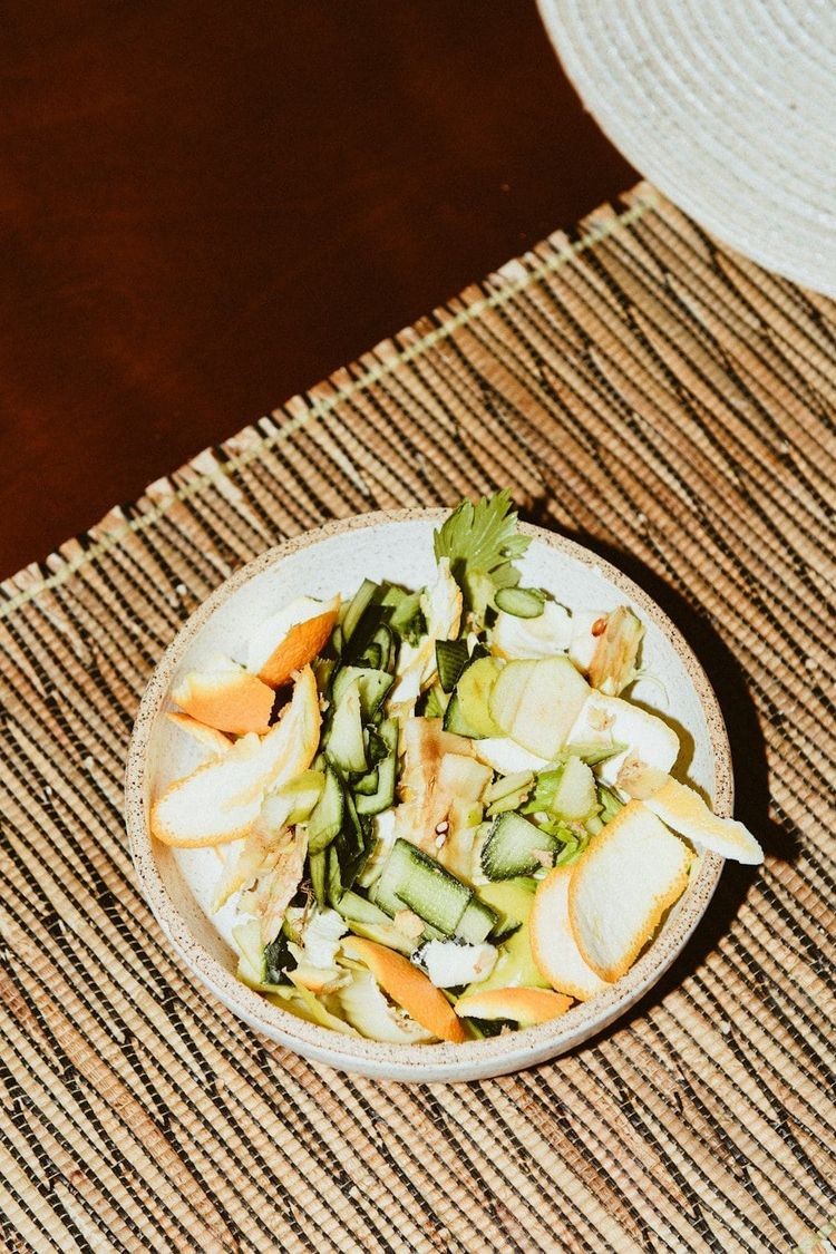 A shallow bowl of vegetable peelings and scraps on a woven table mat
