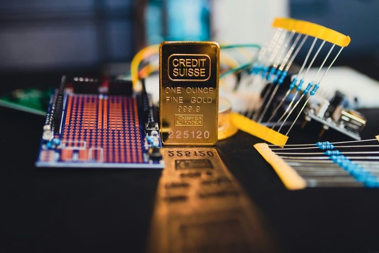 A one ounce gold bar standing among circuit boards and resistors