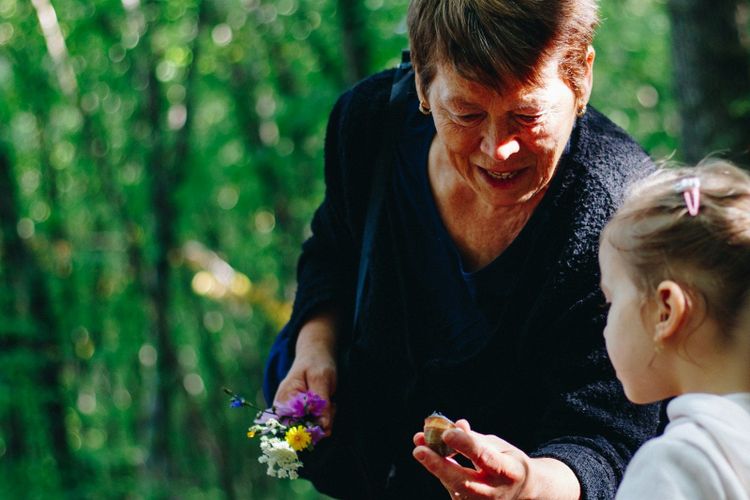 A grandmother in a green wood showing a small girl a posy of wildflowers and a snail