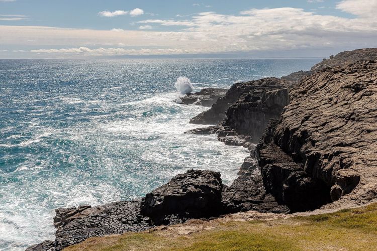 Dark basalt cliffs at Cape Bridgewater with a white blowhole plume bursting out of the turquoise Southern Ocean
