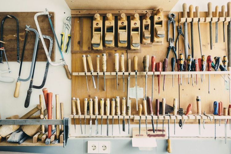 A wall of well kept hand tools hung neatly on a light wooden workshop wall