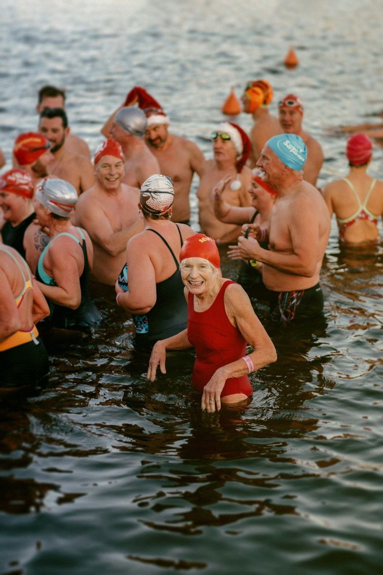 A crowd of ocean swimmers in bright caps, ready for a cold morning dip