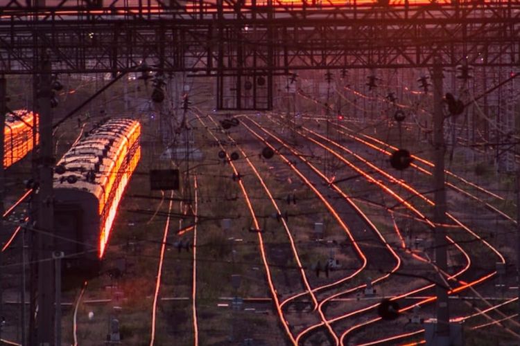 Railway tracks fanning out at sunset, the rails lit orange by low sun