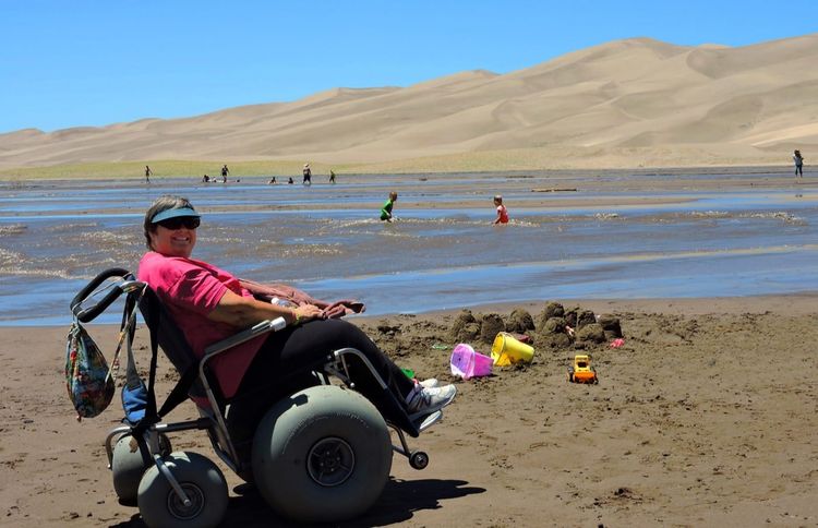 A woman in a beach wheelchair beside a creek at Great Sand Dunes National Park