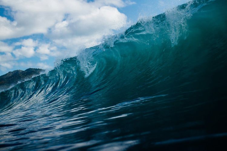 A turquoise ocean wave curling over under a blue sky with white clouds