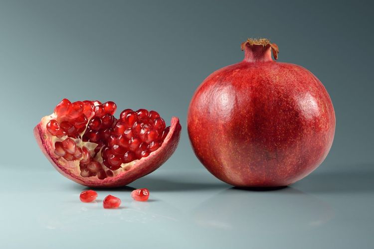 A whole pomegranate beside a cut piece showing the arils inside