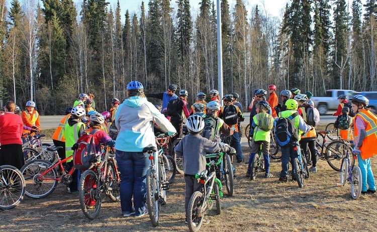 A group of children in helmets and high visibility vests gathered on their bikes before riding to school