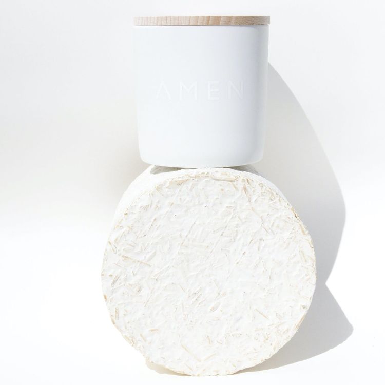 A white candle resting on a round disc of mycelium packaging