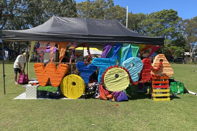 Giant painted letters spelling Woytopia in orange, yellow, blue and pink under a black marquee on a school field