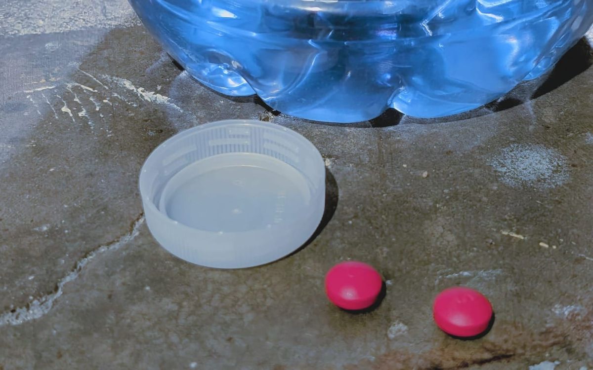 The bottom of a one gallon bottle of water sits on a concrete floor. its bottle cap is discarded and two Tylenol Ultra sit nearby.