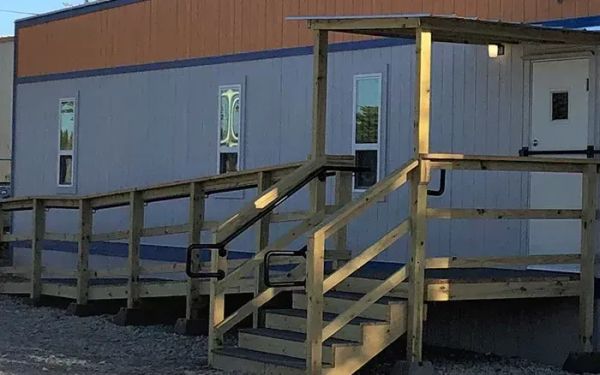 An outdoor modular office with a wood ramp and stair case leading to a white door.