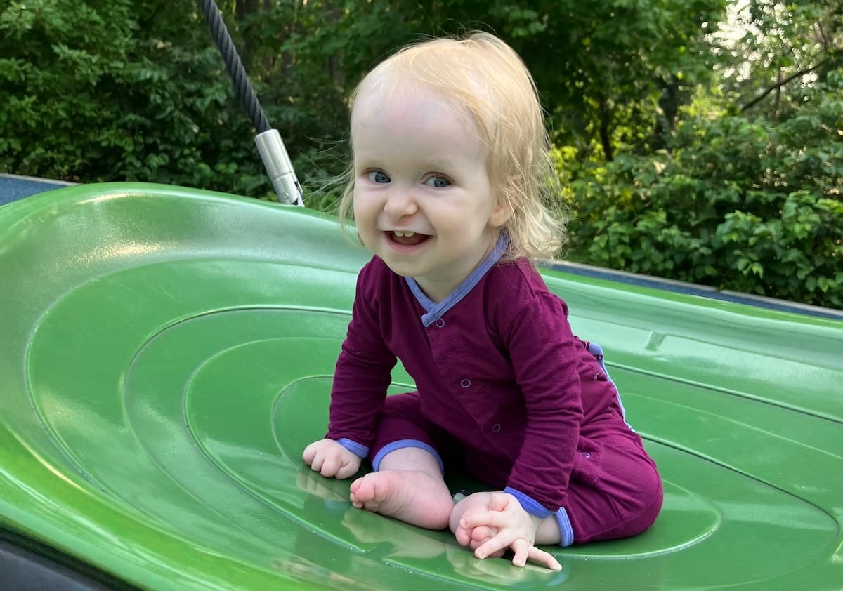 A baby in a red romper smiling. 
