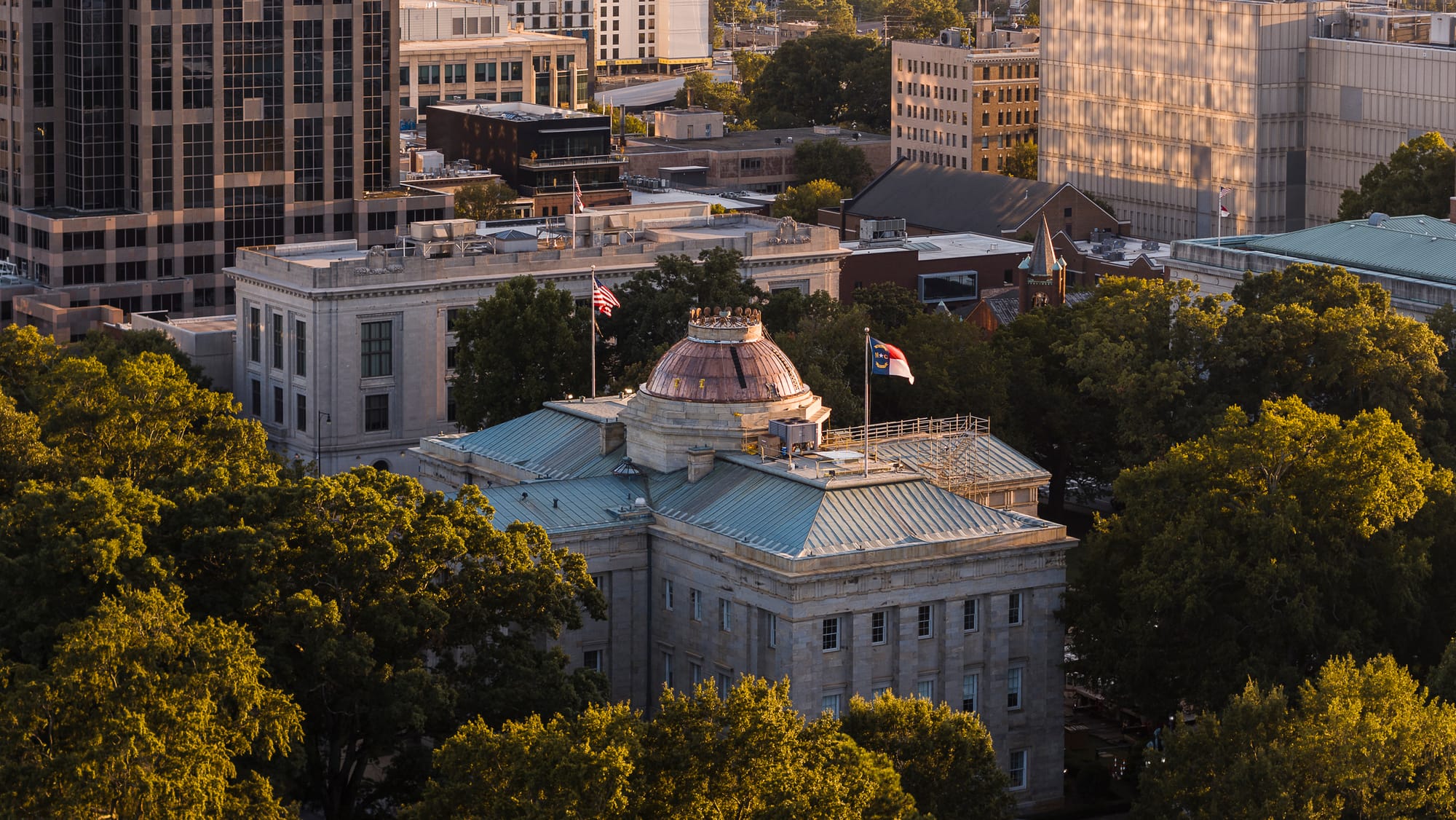 North Carolina State Capitol in Greek Revival style stands surrounded by trees in Downtown Raleigh, NC 