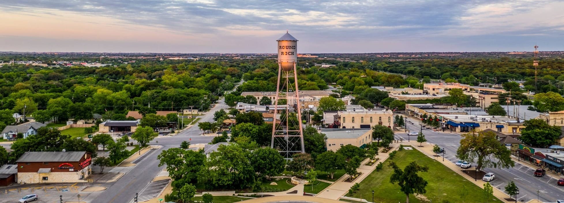 Aerial View of Round Rock. City Water Tower is Centered in the Image with Commercial District and Trees also in the Background. 
