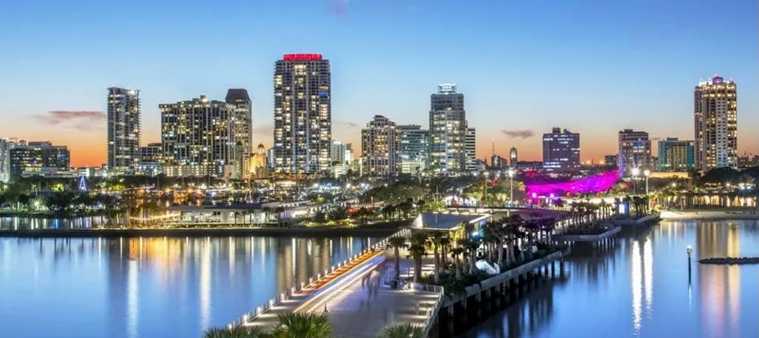 Skyline of St. Petersburg, Florida at sunset. Tall buildings are all lit in the background across the riverside area of the city. 